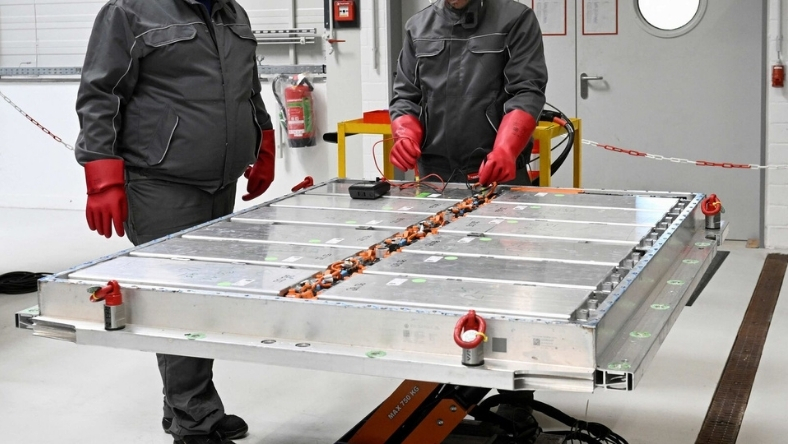 Technicians handling a large battery module in an industrial facility
