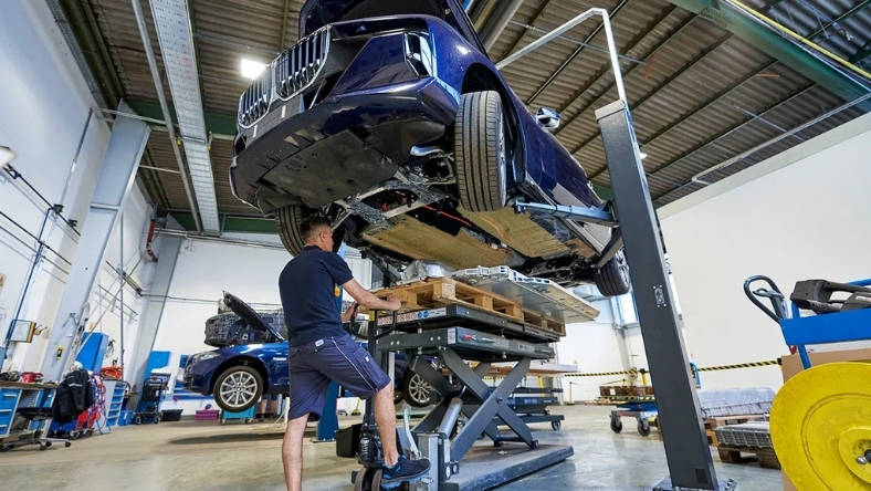 Technician works beneath raised electric vehicle on hydraulic lift inside workshop